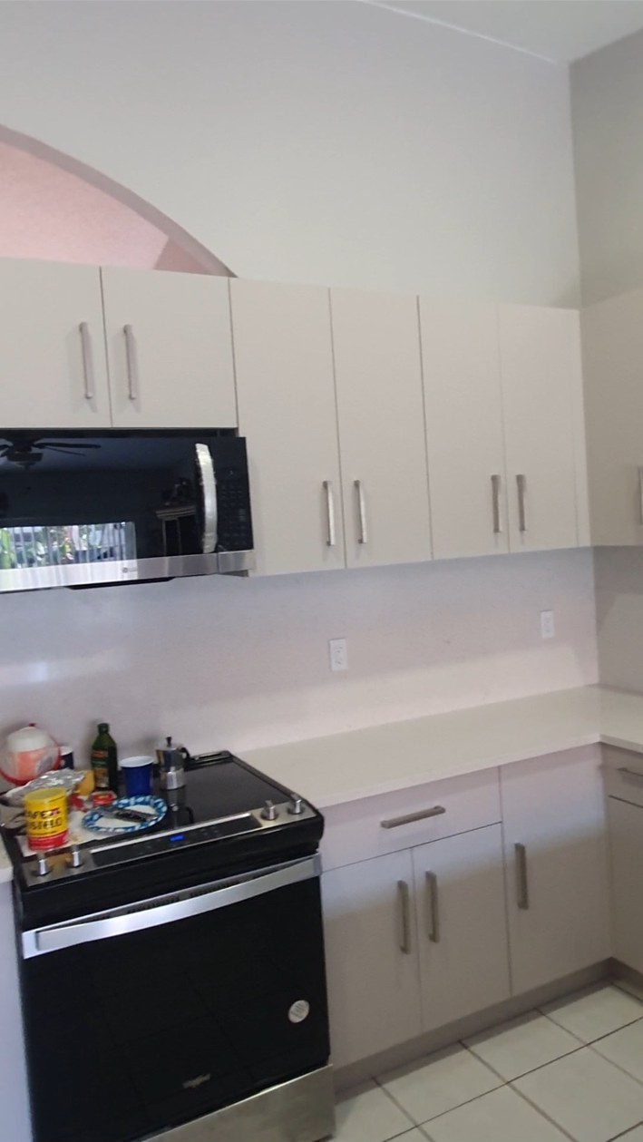 Cocina con gabinetes blancos, encimera clara y electrodomésticos oscuros
