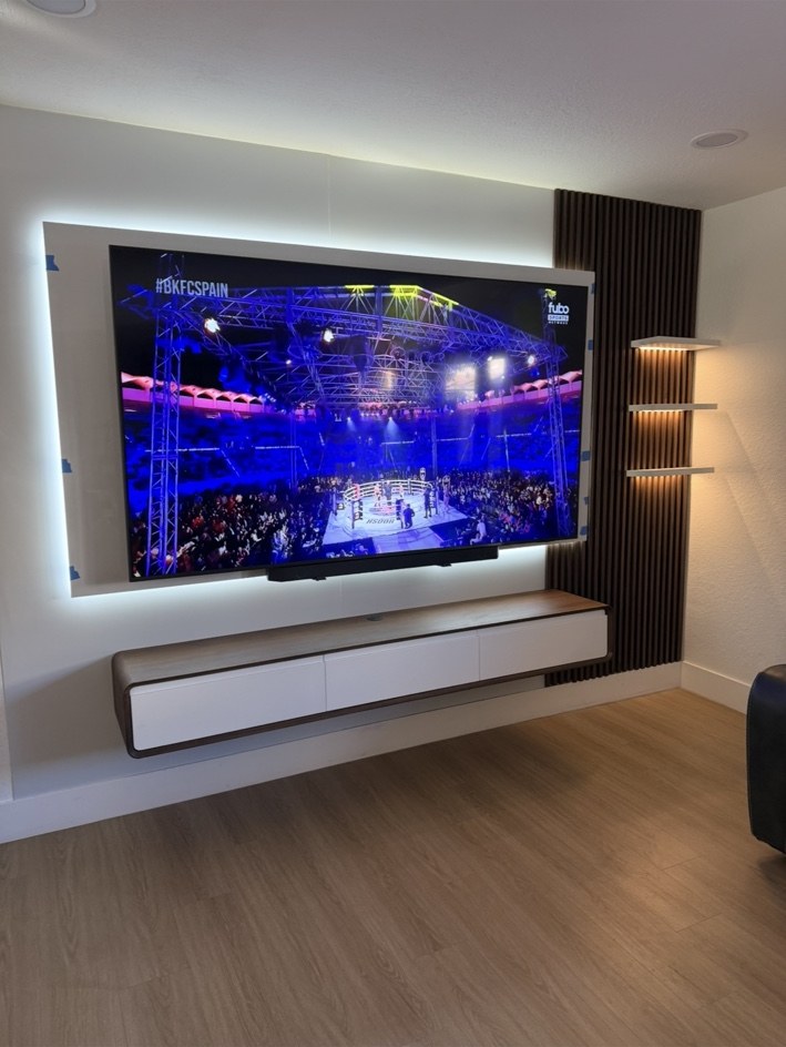 Pared de TV iluminada con gabinete flotante y repisas laterales